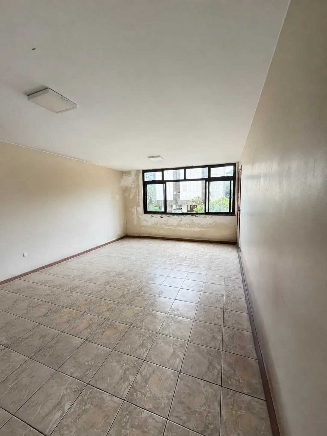 Sala principal ampla, com piso cerâmico e paredes em estado original