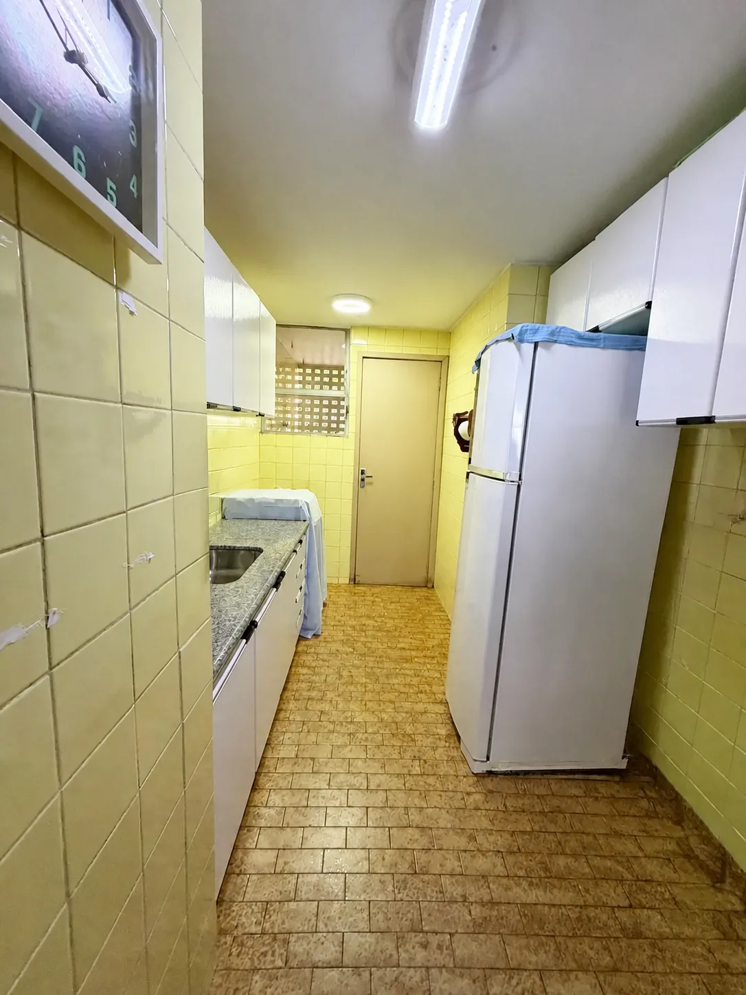 Cozinha em estado original, com armários e área de serviço ao fundo